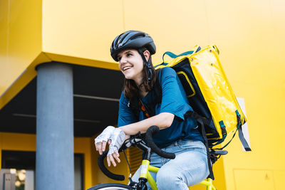 Happy delivery woman with backpack sitting on bicycle