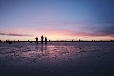 Silhouette people on beach against sky during sunset