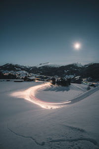 Snow covered road by illuminated city against sky at night