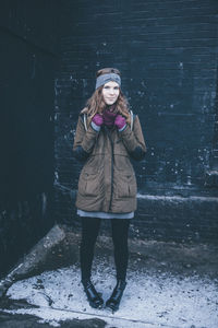 Portrait of beautiful young woman standing against wall during winter