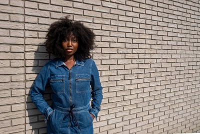 Portrait of young woman standing against brick wall