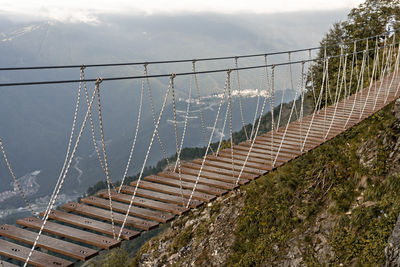 Suspended wooden bridge hanging over an abyss in mountain canyon and clouds, extreme hiking