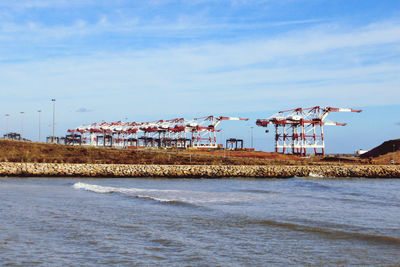 Cranes on beach by sea against buildings against sky