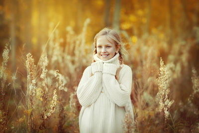 Portrait of a beautiful little girl in a white warm sweater smiling in the autumn forest.