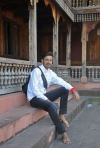 Side view of a male tourist looking at camera while sitting on temple stairs