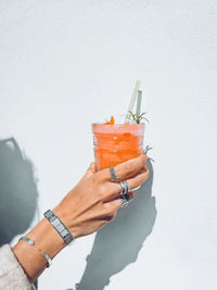 Cropped hand of woman holding drink against white background