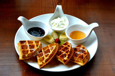 High angle view of waffle and sweet sauce in plate on wooden table