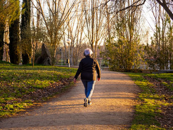 Full length rear view of senior woman walking on footpath in park