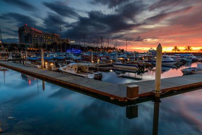 Boats moored at harbor against sky during sunset in city