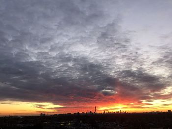 Silhouette of city against dramatic sky during sunset