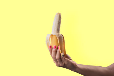 Midsection of person holding ice cream against yellow background