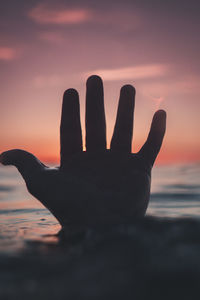 Silhouette hand against sky during sunset