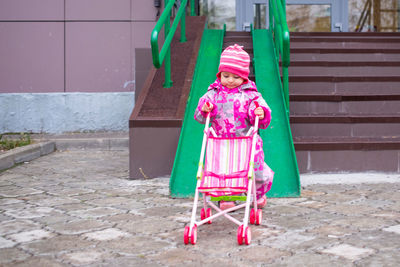 Toddler drags a toy stroller along the ramp of the stairs