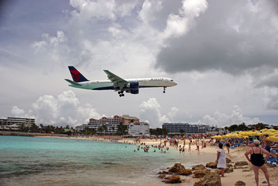 Airplane flying over people against sky