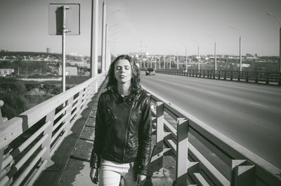 Young woman with eyes closed walking on bridge against sky