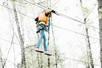 Low angle view of girl walking on rope in forest