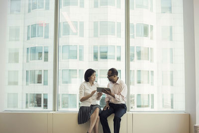 Business people with digital tablet sitting on window sill, discussing