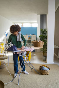 Young woman with clothes at ironing board in living room