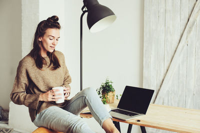 Woman having drink with laptop at table