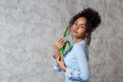 Portrait of smiling young woman holding tulip while standing against wall