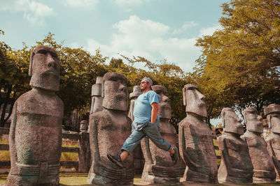 Man jumping while walking in air by statues against sky