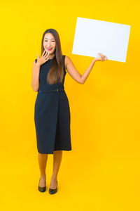 Full length portrait of woman standing against yellow background