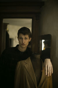 Portrait of young man puckering while leaning on mannequin with blazer at home