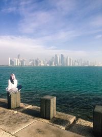 Rear view of woman sitting on bollard at promenade against city