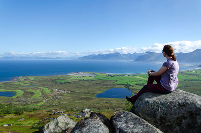 Rear view of woman sitting on rock against sky