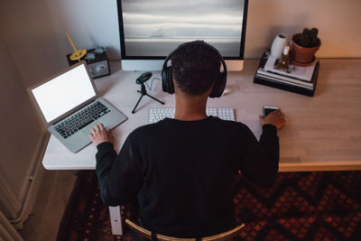 High angle view of young freelance worker using laptop and computer at desk