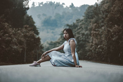 Side view of young woman sitting against trees