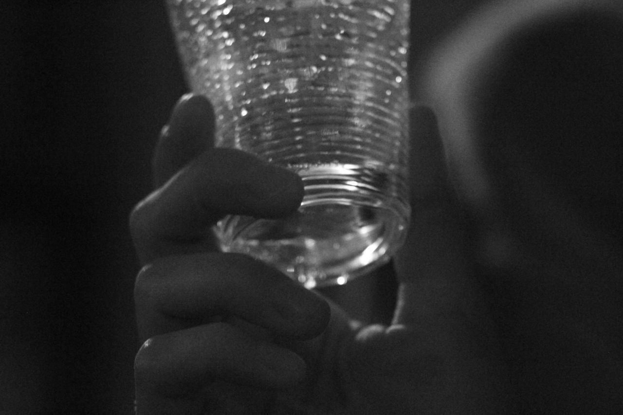 CLOSE-UP OF HAND HOLDING GLASS OF BLACK BACKGROUND