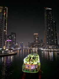 Illuminated modern buildings by river against sky in city at night