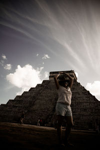 Low angle view of man standing against cloudy sky