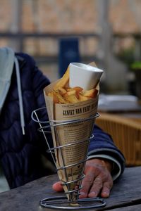 Midsection of woman holding a paper cone with fries. 