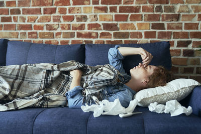 Portrait of young woman lying on sofa against wall