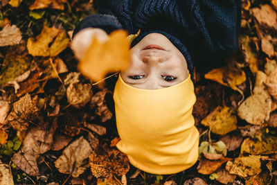 Close up portrait of a boy a child in a hat holding an fall leaf and lying in the fall park outdoor