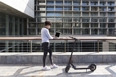 Young man with e-scooter using laptop in the city