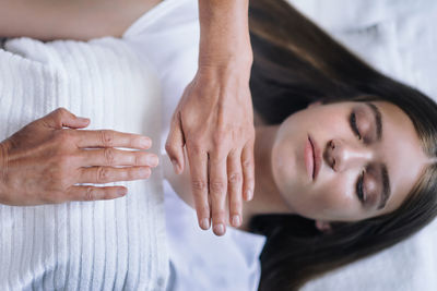 Cropped hands of therapist giving reiki treatment to teenage girl on face at spa