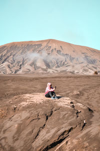 Man sitting on desert against clear sky