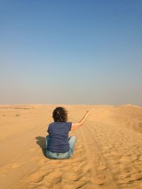 Rear view of woman sitting on desert
