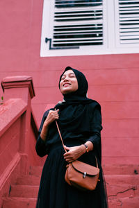 Young woman looking away while standing against wall