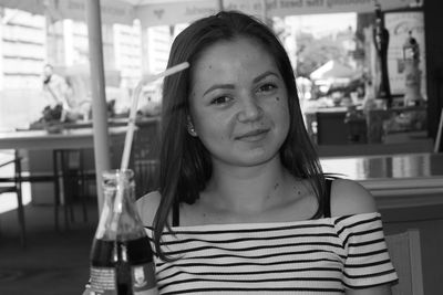 Portrait of young woman with drink on table at restaurant