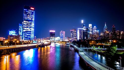 Illuminated buildings by river against sky at night