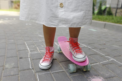 Girl with pink skateboard standing on footpath