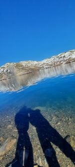 Shadow of people on shore against clear blue sky