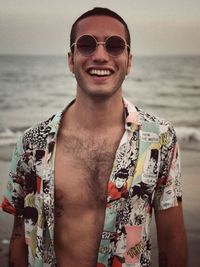 Portrait of happy young man wearing sunglasses at beach