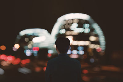 Rear view of man standing against illuminated buildings in city