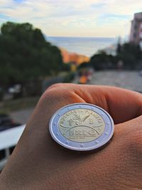 Close-up of coin on hand with sea in background