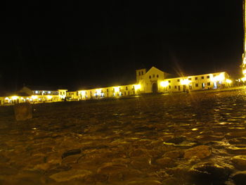 Illuminated houses by sea against sky at night